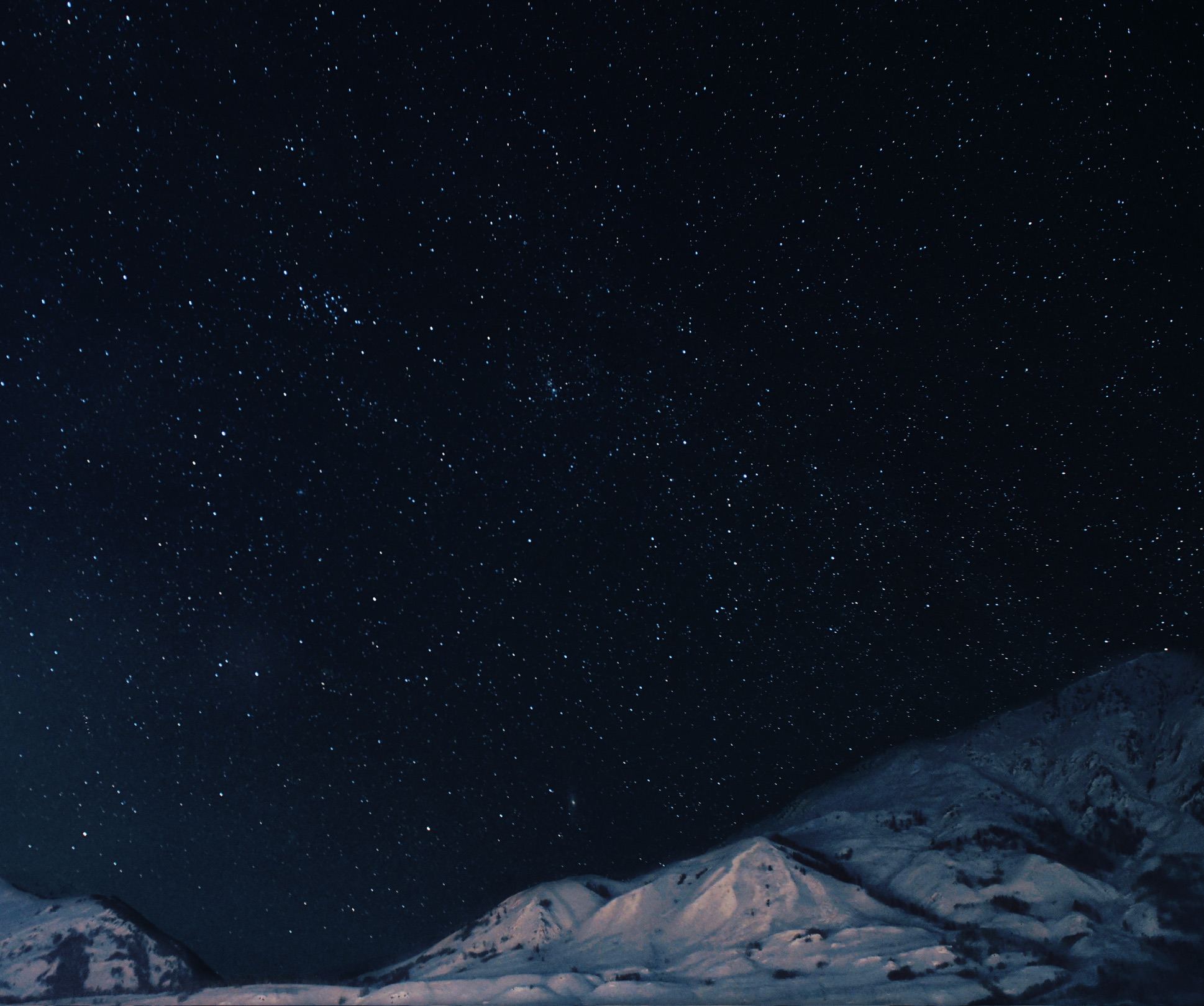 A star-filled night sky over snow-covered mountain ridges