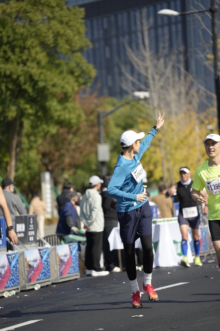 Jackson in a white cap and blue running shirt flashing a peace sign while running a marathon