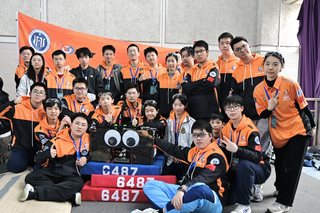 The full FIRST Robotics team posing with the competition robot behind a 6487 banner