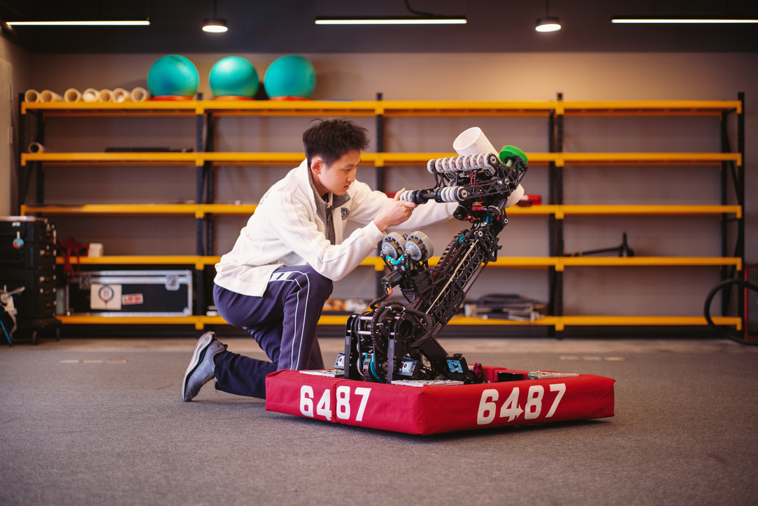 Jackson kneeling in the workshop adjusting the arm mechanism of the FRC robot